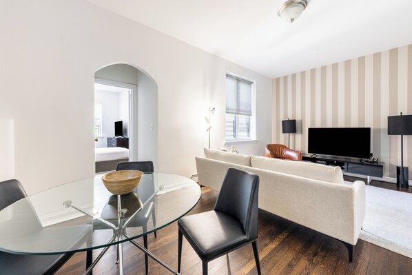 A modern living room with a glass dining table, leather sofa, and a flat-screen TV.