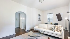 Un salon moderne avec une table basse en verre, un canapé blanc et une grande fenêtre.