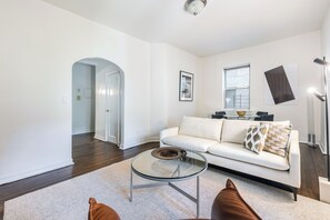 A modern living room with a glass coffee table, a white sofa, and a large window.