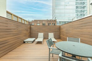 Una terraza en la azotea con suelo de madera, dos sillones, una mesa y una silla.