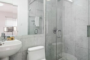 Un baño con cabina de ducha de vidrio, un lavabo blanco y un inodoro.