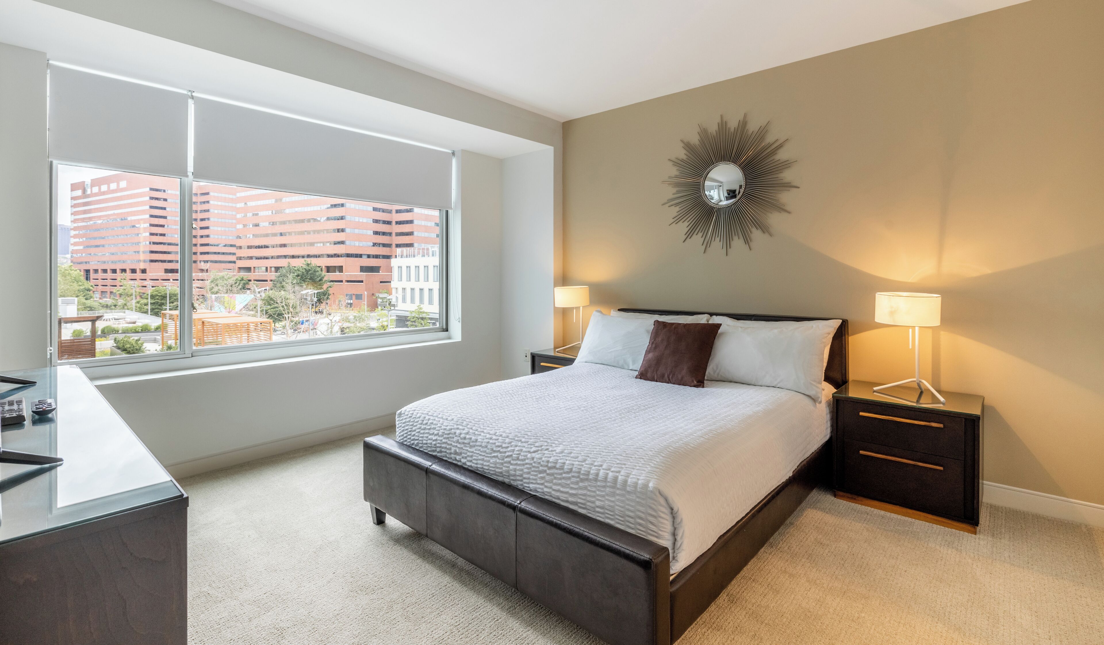 Um quarto moderno com uma janela grande, uma cama com duas mesas de cabeceira e um espelho fixado na parede.