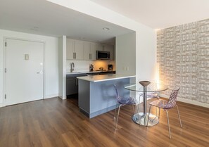 A modern kitchen with white cabinets, a microwave, and a glass island. There are two glass chairs and a small round table.