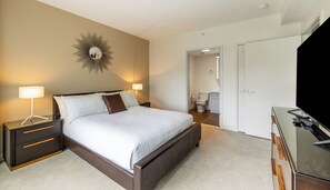 Quarto moderno com cama, mesas de cabeceira, espelho e televisão.