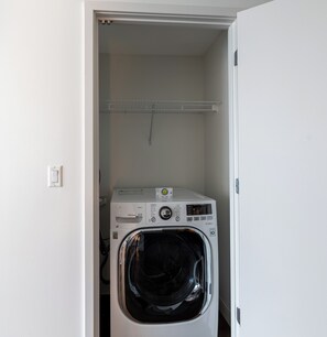 A compact laundry room with a front-loading washing machine and a drying rack above.