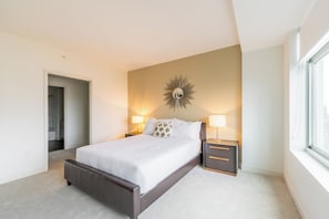 A modern bedroom with a large bed, bedside lamps, a decorative wall piece, and a window.