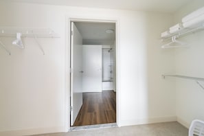 Een kamer met een houten vloer, witte wanden, een deur naar een badkamer en een witte wasrek.