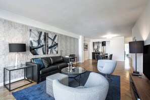 A modern living room with a black leather sofa, a grey armchair, a glass coffee table, and a large abstract painting on the wall. - Elegant Murray Hill | Fitness Center & Laundry (New York)
