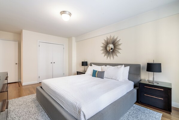 A bedroom with a large bed, a nightstand with a lamp, a wardrobe, and a decorative mirror on the wall.