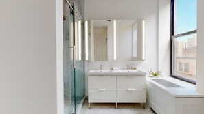 Un baño moderno con cabina de ducha de vidrio, tocador doble y un espejo grande.