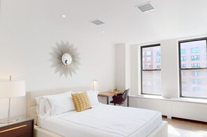 Una camera d'albergo moderna con un letto grande, una scrivania e vista sugli edifici dalle finestre.