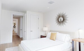 Un dormitorio moderno con una cama grande, una mesita de noche con lámpara y un espejo decorativo en la pared.