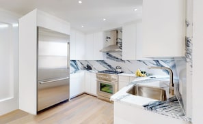 Una cucina moderna con pensili bianchi, un frigorifero in acciaio inossidabile, un piano cottura a gas e una schiena di marmo.