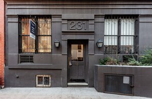 A building with a black facade, numbered 281, featuring a black door, two windows with metal bars, and a small air vent. - Live Local | Chelsea | Pet-Friendly & W/D (New York)