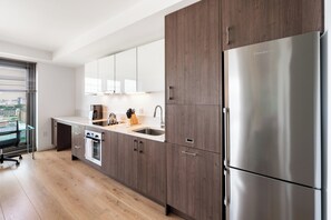 Une cuisine moderne avec des meubles en bois, un réfrigérateur en acier inoxydable et une vue sur la ville par la fenêtre.