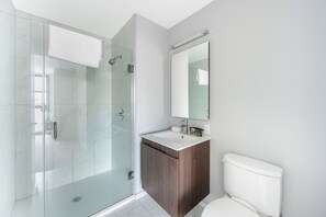 Un baño moderno con ducha envuelta en vidrio, tocador de madera y retrete blanco.