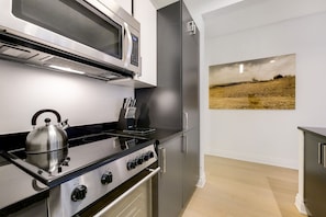 A modern kitchen with stainless steel appliances, a kettle on the stove, and a painting on the wall. - Spacious Studio In Downtown NYC (New York)