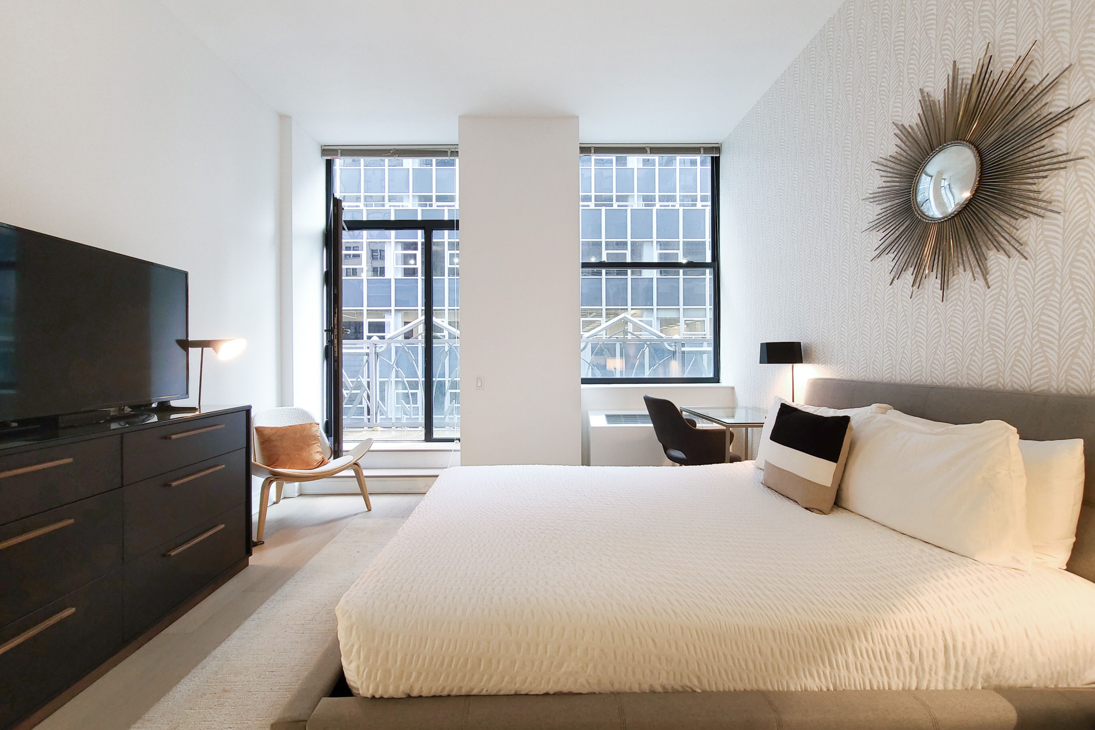 A modern hotel room with a large bed, a TV, a desk, and a chair.