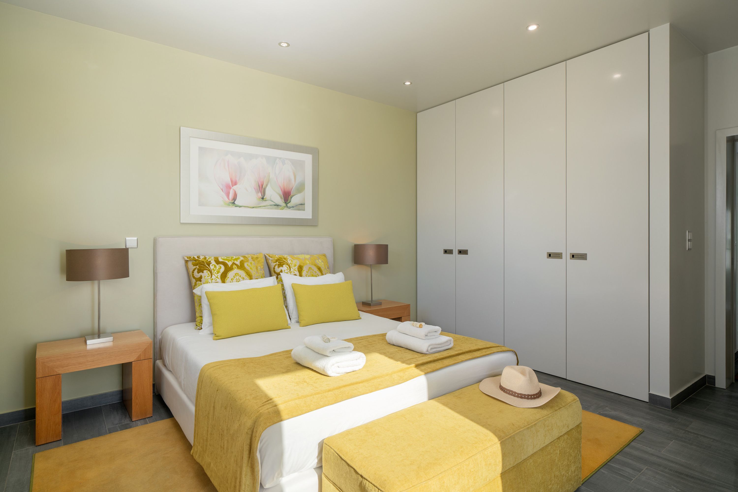 Um quarto moderno com uma cama grande, mesas de cabeceira, um guarda-roupa e uma obra de arte floral emoldurada na parede.