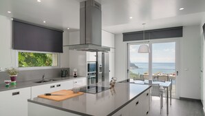 Une cuisine moderne dotée d’un grand îlot central, d’appareils électroménagers en acier inoxydable et offrant une vue sur la mer.