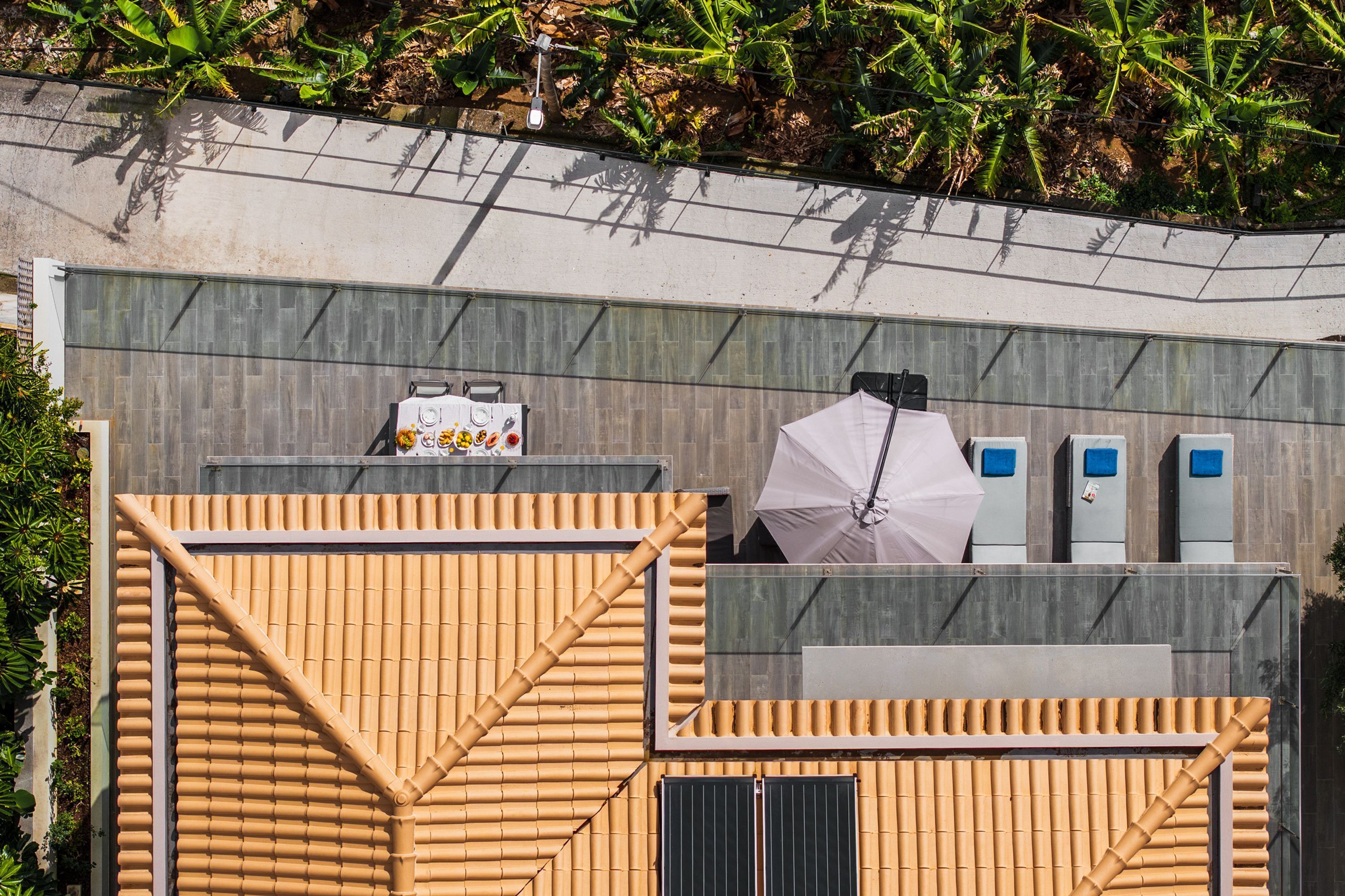 Un edificio moderno con fachada de bambú, un pequeño espacio al aire libre con sombrillas y una pared gris con una ventana.