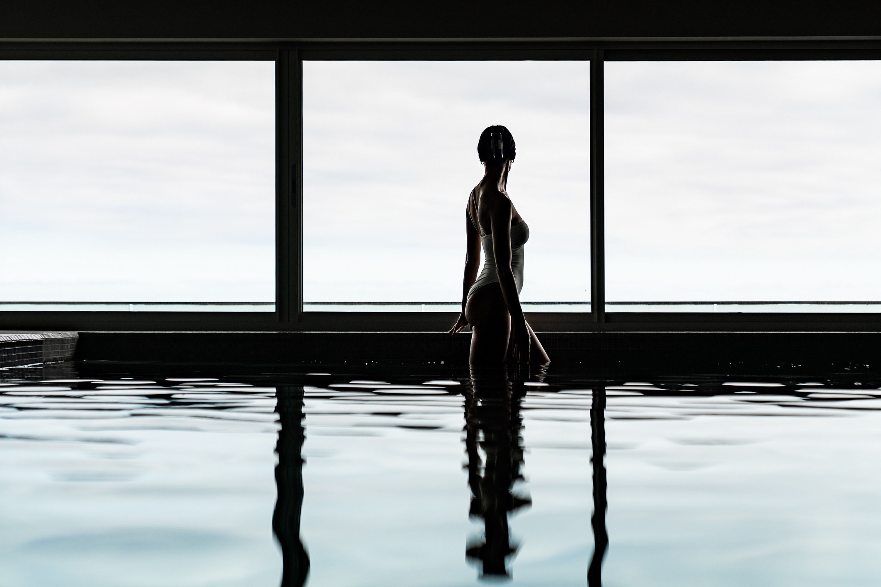 A person standing in a room with large windows and a reflective floor.