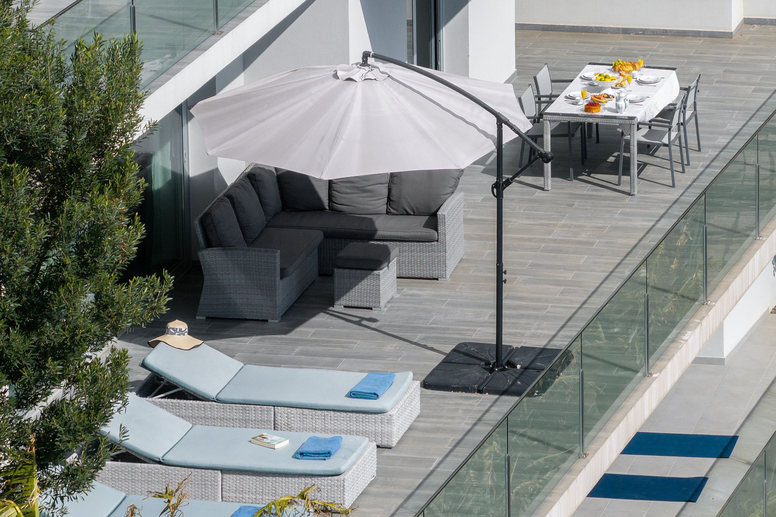 Une terrasse sur le toit, dotée d’un espace salon, d’une table dressée pour les repas et d’un grand parasol offrant de l’ombre.