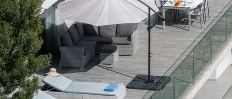 Une terrasse sur le toit, dotée d’un espace salon, d’une table dressée pour les repas et d’un grand parasol offrant de l’ombre.