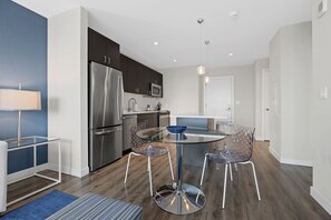 A modern kitchen with stainless steel appliances, a glass dining table, and contemporary chairs. - Gorgeous One Bed in Amenity-Rich Community (Boston)