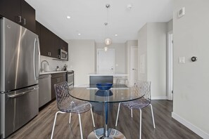 A modern kitchen with stainless steel appliances, a glass dining table, and clear chairs. - Gorgeous One Bed in Amenity-Rich Community (Boston)