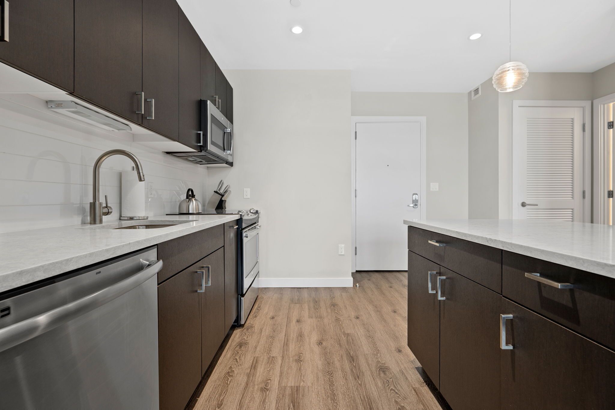 A modern kitchen with dark cabinetry, stainless steel appliances, and a wooden floor.