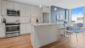 Et moderne køkken med rustfrie stålapparater, en glasø med spiseplads og en blå stol.