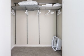 Un armario empotrado con estantes metálicos, perchas blancas y una cesta de ropa blanca.
