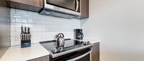 Una cocina moderna con una campana extractora de acero inoxidable, un microondas, un hervidor y una cafetera.