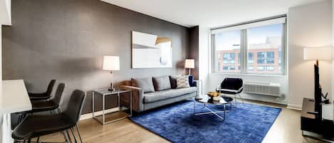 A modern living room with a sofa, coffee table, and chairs, a large window with a city view, and a blue rug.