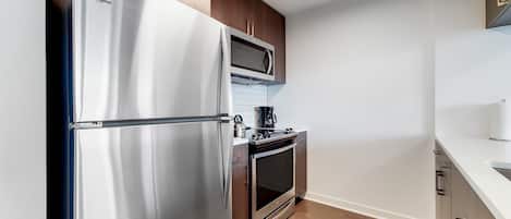 A modern kitchen with stainless steel appliances, wooden cabinets, and a white countertop.