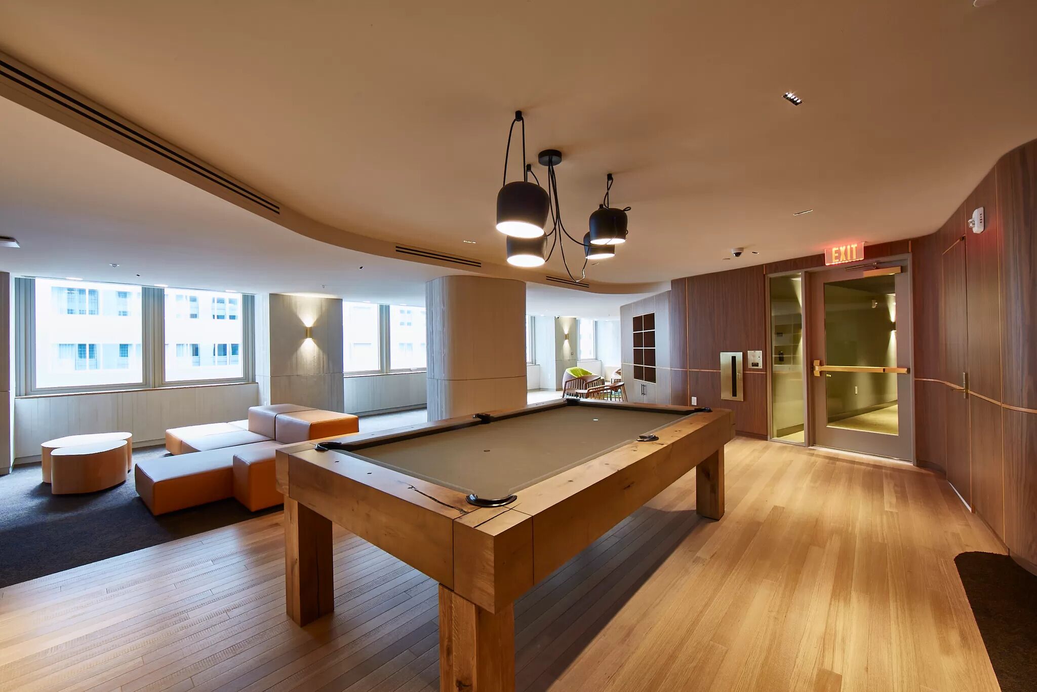 Una mesa de billar moderna en una habitación bien iluminada con ventanas amplias, un sofá y un mueble de madera.