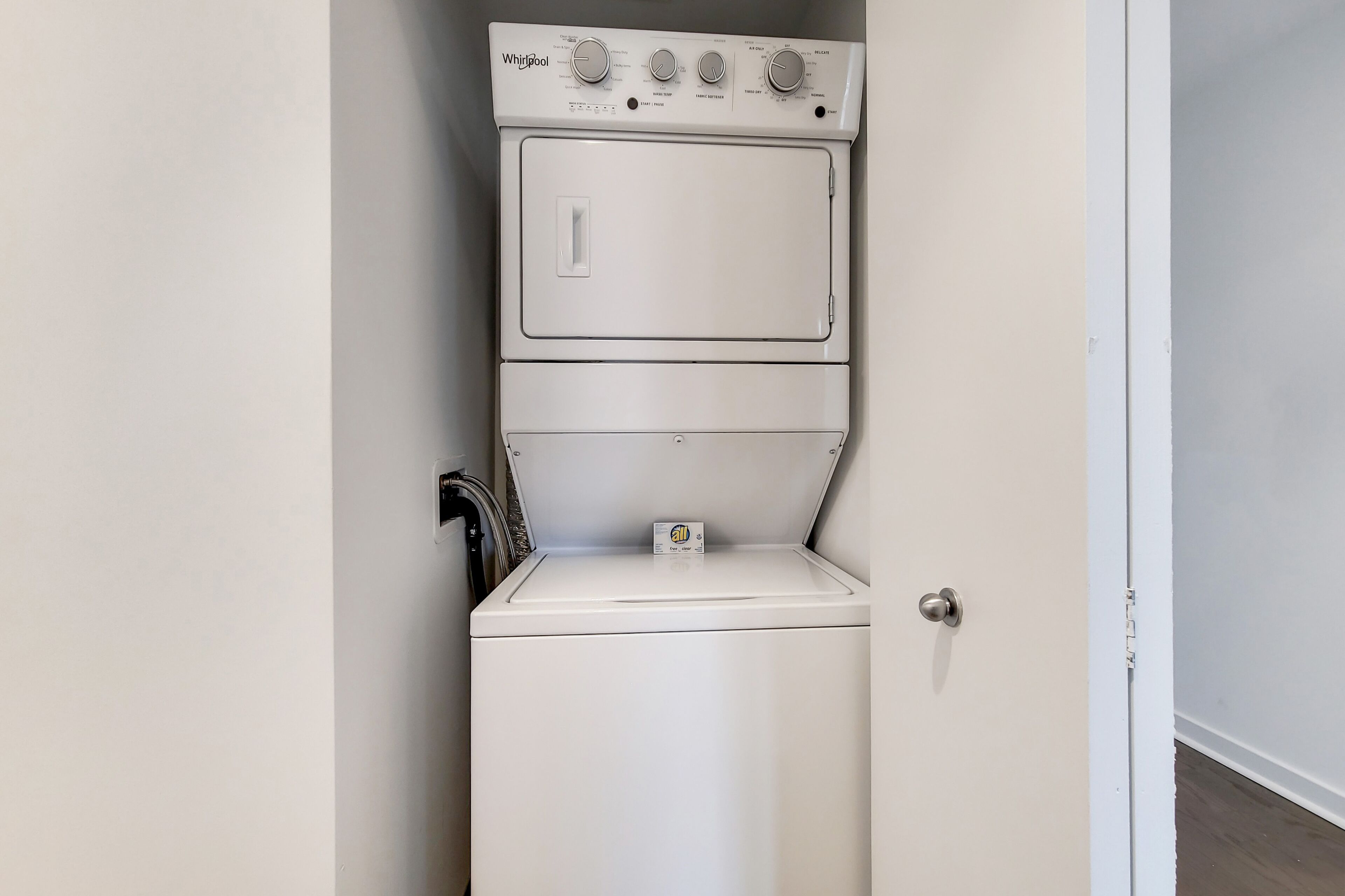 Una lavadora y secadora Whirlpool blancas y compactas en una habitación pequeña con una puerta a la derecha.