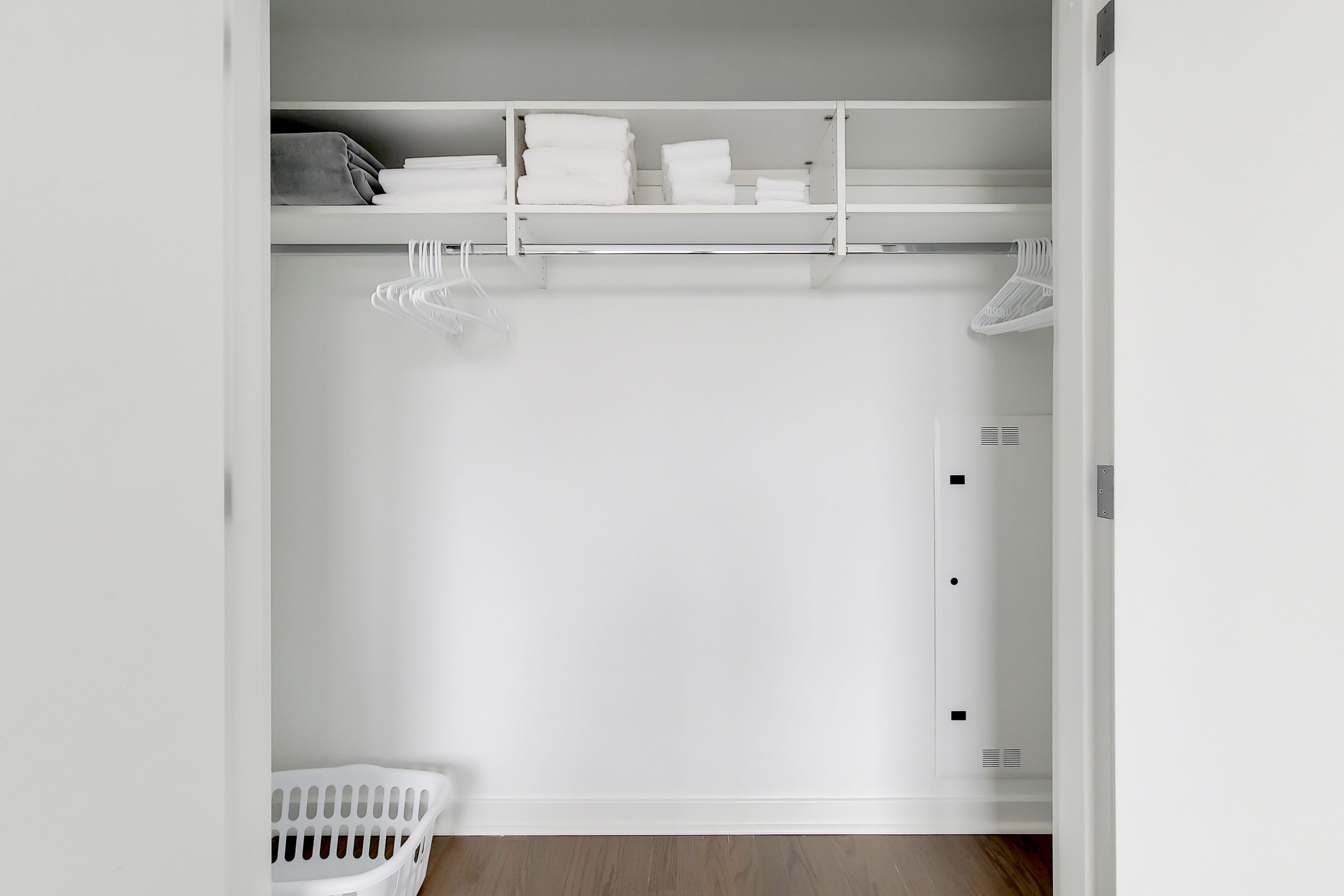 Un placard blanc avec des étagères, une tringle pour suspendre les vêtements et un panier à linge.