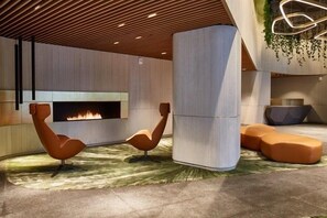 A modern lobby with a fireplace, two unique chairs, and a seating area with cushions. - Professionally Designed One Bedroom In Jersey City (Jersey City)