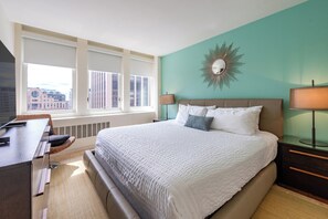 Enjoy a city view from the large window with blinds, featuring a comfortable bed and a convenient desk with chair.