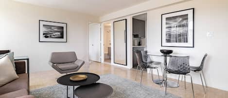 A modern living room with a sofa, a chair, a small table, and a dining area with chairs and a table.