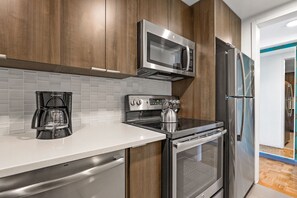 A modern kitchen with stainless steel appliances, a coffee maker, and wooden cabinets. - Boston One Bed With Luxury Building Amenities (Boston)