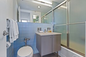 A bathroom with a toilet, a sink with a mirror above it, and a shower with frosted glass doors.
