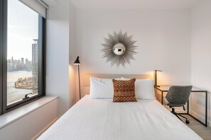 Een moderne hotelkamer met een groot bed, uitzicht over de stad, een decoratieve spiegel en een bureau met een stoel.