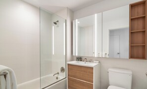 Een moderne badkamer met een glazen douchecabine, een witte badkuip, een houten wastafelmeubel met een wastafel en een toilet.