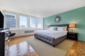 A bedroom with a large bed, two bedside lamps, a city view, and a modern decor.
