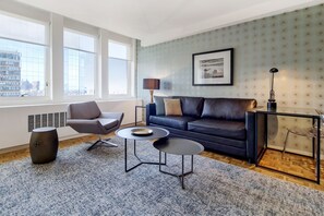 A modern living room with a leather sofa, two round tables, a side table, and a large window with a city view.
