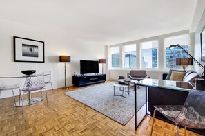 A modern living room with a flat-screen TV, a glass dining table, and a sofa.
