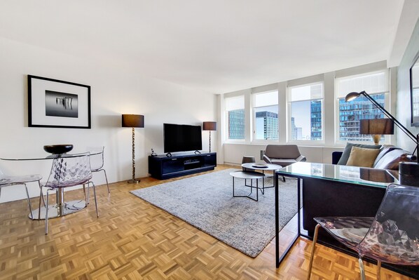A modern living room with a flat-screen TV, a glass dining table, and a sofa.